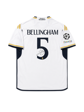 2023-24シーズンのレアル・マドリード ホームユニフォーム。白地にネイビーとゴールドのアクセント、背面のBELLINGHAMと5番、シグネチャープリント、欧州大会仕様パッチ入り。