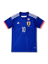 日本代表 2014 ホームジャージの正面、ジャパンブルーボディ、JFAエンブレム、日本国旗パッチ、ホワイト肩ライン、レッド袖口、漫画グラフィック入り10番が見えるデザイン