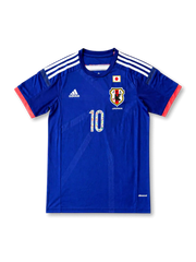 日本代表 2014 ホームジャージの正面、ジャパンブルーボディ、JFAエンブレム、日本国旗パッチ、ホワイト肩ライン、レッド袖口、漫画グラフィック入り10番が見えるデザイン