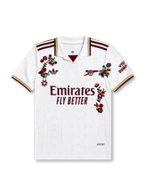 アーセナルFC2025-26サード手刺繍カスタムジャージ正面、純白地にハイベリーアールデコ建築ジャカードパターン、ポロカラー・マルーンV差し色・ゴールド3色リブ、両肩マルーン&ゴールド3ストライプス、左胸マルーンadidas Originalsトレフォイルロゴ、右胸シンプル化キャノン紋章、右袖Visit Rwanda、中央マルーンEmirates Fly Betterスポンサー、左右にイングリッシュローズ&ピンク小花&白マーガレットの英国伝統花柄ハンド刺繍
