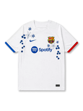 FCバルセロナ2023-24アウェイ手刺繍ジャージ正面、白地にブルーのスウッシュとF.C.Bエンブレム、Spotifyスポンサー、左青・右赤の非対称カフ、胸に青と白の花々と星形の花の立体的な刺繍