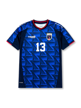 カーボベルデ代表2026-27ホームユニフォーム前面・ロイヤルブルーとネイビーの幾何学トライアングル柄、ネイビー×レッドのVネックと袖トリム、中央に白の背番号13、左胸Capelli Sportロゴ、右胸にサメのFCFエンブレム