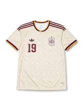 スペイン代表 2026 ワールドカップ アウェイ レプリカユニフォーム フロント、生成りボディに渦巻きオーナメント調トーナル総柄、右胸にバーガンディ1色のスペイン連盟エンブレムと星、左胸にトレフォイルロゴと胸番号19、バーガンディと金のVネックと肩3ストライプ