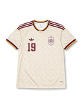 スペイン代表 2026 ワールドカップ アウェイ レプリカユニフォーム フロント、生成りボディに渦巻きオーナメント調トーナル総柄、右胸にバーガンディ1色のスペイン連盟エンブレムと星、左胸にトレフォイルロゴと胸番号19、バーガンディと金のVネックと肩3ストライプ