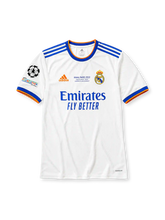 ホワイトベースにブルー×オレンジの襟と袖口ラインを配し、右袖にUEFAチャンピオンズリーグ13度優勝エンブレムとUEFAファウンデーションパッチを備え、背面にブルーのBENZEMAネームと9番、その下にレアル・マドリードのクラブエンブレムをあしらったレアル・マドリード2021-22ホームジャージ背面