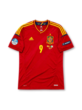 レッドベースに肩のイエロー3本ラインとネイビー袖口ラインを配し、胸にadidasロゴ、星付きスペインサッカー連盟エンブレム、イエローの9番、決勝戦カード(スペインvsイタリア 2012年7月1日キエフ)表記、左袖にUEFAユーロ2012優勝エンブレム、右袖にRESPECTパッチ、裾にCLIMACOOL表記を備えたスペイン代表2012ユーロ決勝記念ホームジャージ正面