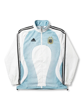 アルゼンチン代表 2006 トラックジャケット adidas 正面 — ホワイト×スカイブルー同心円ウェーブ、2つ星AFAゴールドエンブレム、ブラック3ストライプ