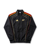 アーセナル × adidas × NTS トラックジャケット ブラック 前面 — 炎色三層ストライプとゴールドキャノン刺繍を配した三者構成コラボモデル