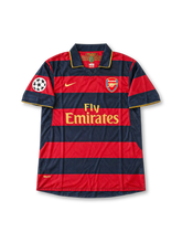 アーセナルFC 2007-08シーズン サードユニフォーム デニス・ベルカンプ10番のトリビュートモデル Nike製 ネイビーとワインレッドの太い横ボーダー柄、ゴールドの縁取りを施したポロカラーと袖口、ゴールドのNikeスウッシュとFly Emiratesスポンサーロゴ、クラブエンブレム、UEFAチャンピオンズリーグの袖章、背面にBERGKAMPのネームと10番を配したレトロサッカージャージ