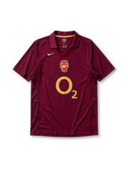 レッドカラント地にゴールドパイピングのポロ襟、左胸のゴールドNikeスウッシュ、中央のHIGHBURY 1913-2006記念エンブレム、大きなO2スポンサーロゴ、両脇のメッシュ通気パネルを備えたアーセナル2005-06ホームジャージ正面