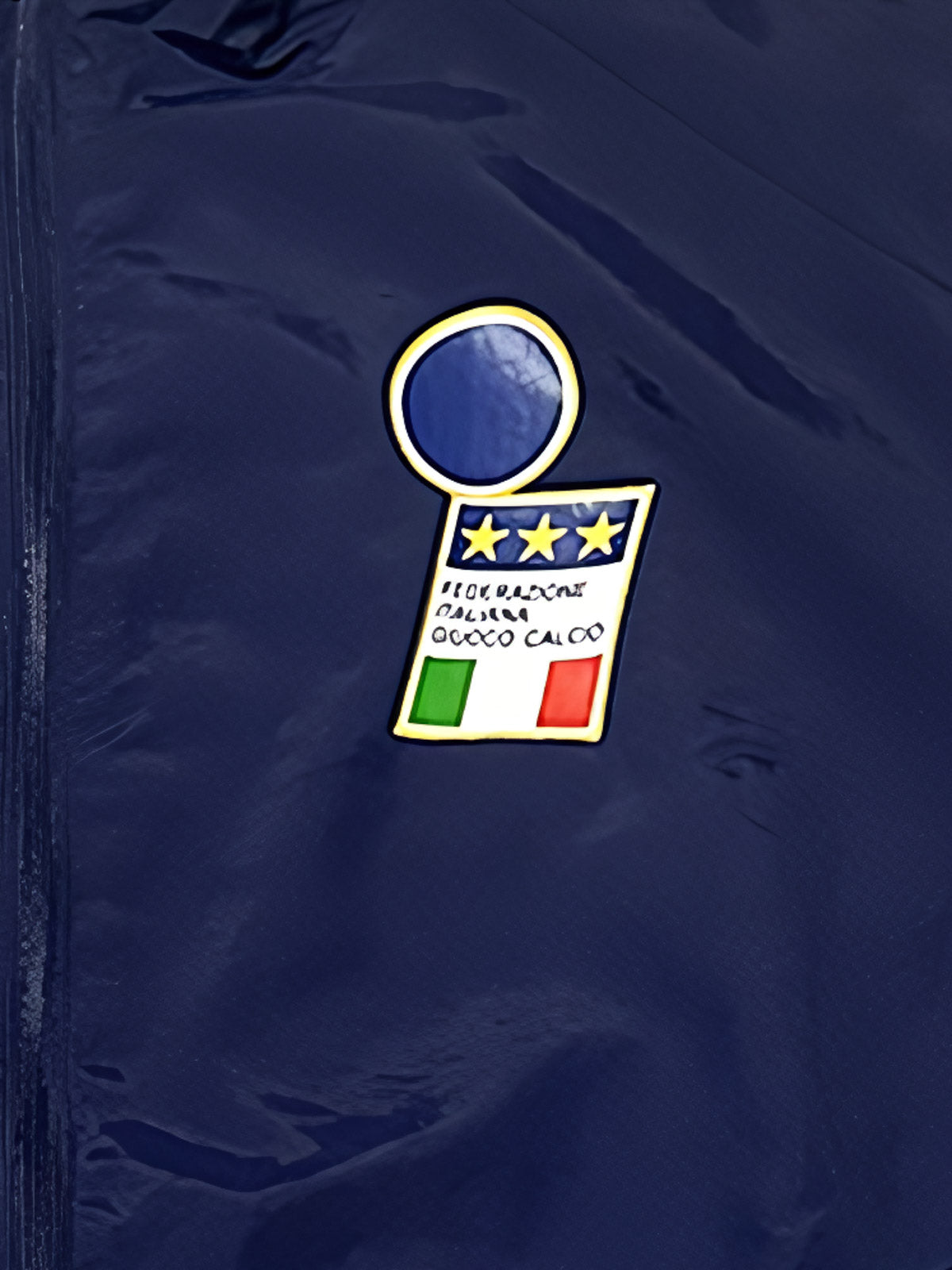 詳細画像1：胸元に配置された高品質刺繍のイタリア代表エンブレムとAdidasトレフォイルロゴのクローズアップ。ワールドカップ準優勝時代のクラシックなスタイルを表現。
詳細画像2：袖部に施されたグリーン・ホワイト・レッドの国旗三色ストライプデザインの特写。イタリアの民族性とサッカー文化を強調したディテール。
詳細画像3：袖口と裾部分の仕上げディテールのクローズアップ。軽量防風素材を採用し、快適性と実用性を兼ね備えたデザイン。