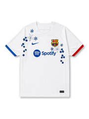 FCバルセロナ2023-24アウェイ手刺繍ジャージ正面、白地にブルーのスウッシュとF.C.Bエンブレム、Spotifyスポンサー、左青・右赤の非対称カフ、胸に青と白の花々と星形の花の立体的な刺繍