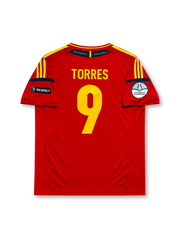 レッドベースに肩のイエロー3本ラインとネイビー袖口ラインを配し、胸にadidasロゴ、星付きスペインサッカー連盟エンブレム、イエローの9番、決勝戦カード（スペインvsイタリア 2012年7月1日キエフ）表記、左袖にUEFAユーロ2012優勝エンブレム、右袖にRESPECTパッチ、裾にCLIMACOOL表記を備えたスペイン代表2012ユーロ決勝記念ホームジャージ正面